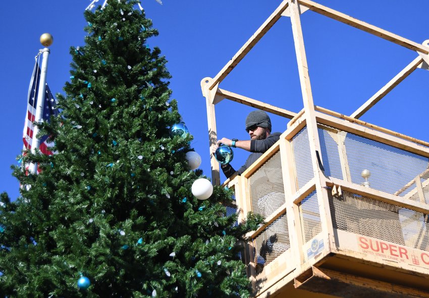Bo Luker with First Security Bank uses a skylift Wednesday to decorate the top part of the giant Christmas tree on display  at the Veterans Plaza in downtown Mountain Home. First Security Bank workers and members of the Mountain Home Street Department spent parts of the week decorating the Veterans Plaza for the Mountain Home Area Chamber of Commerce's Christmas parade and downtown festival, which will be held Friday evening.