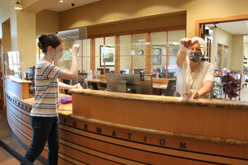 Members of the Baxter County Library staff set up plastic glass dividers atop the library's circulation desk. The dividers were purchased with a purchased with a grant from the Arkansas Community Foundation.