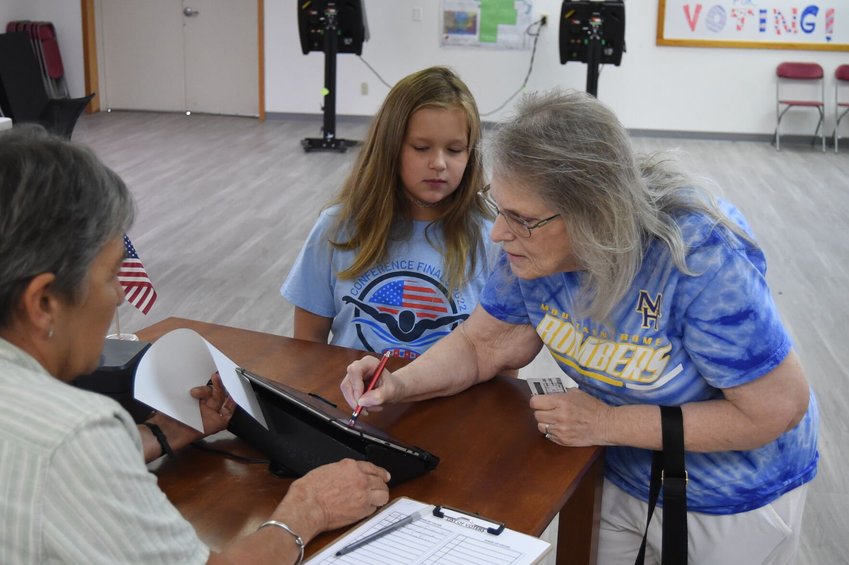 Lylah Campbell, who will be in the fourth grade when school resumes later this month, watches as her great-grandmother Patricia Calhoun signs in to vote Tuesday at the Baxter County Election Commission Headquarters. Also seen in the above photo is poll worker Libby Stewart (far left).   Scott Liles/The Baxter Bulletin