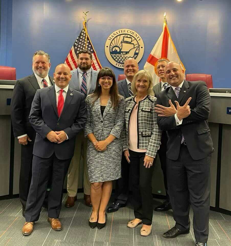 Anthony Pedicini poses in BOCC chambers following the Nov 2022 commissioner swearing-in ceremony. Pedicini was hired by each of Manatee County's current commissioners during their campaigns and proudly displays seven fingers representing the election victories. (Back Row) Left/Right: District 4 Commissioner Mike Rahn, District 1 Commissioner James Satcher, At-Large Commissioner Jason Bearden, At-Large Commissioner George Kruse. (Front Row) Left/Right: District 3 Commissioner Kevin Van Ostenbridge, District 2 Commissioner Amanda Ballard, former District 5 Commissioner Vanessa Baugh, SIMWINs Political Consultant Anthony Pedicini