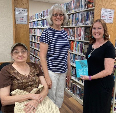 Author Kelly I. Hitchcock, right, holds a copy of her recently published book &ldquo;Community Klepto.&rdquo; A former Buffalo resident, Hitchcock stopped by the Dallas County Library on Saturday morning, July 16, and is pictured with two of her former Buffalo teachers, Ray Dean Phillips, left, and Claire Holt, middle.