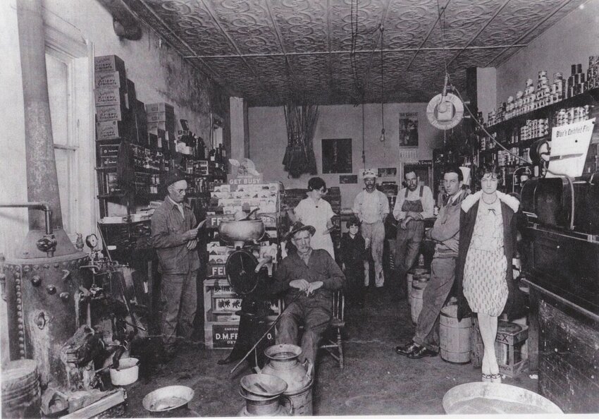 A gathering at Hood's Store on the west side of Main Street, in 1927, (l/r) Ward Harmon, Charley Day, Stella Hood, Virginia Hood, Toby Schwarzenbach, Charles Hood, Velie Hood and Oletes Hood. Steam boiler on left was used in processing cheese on the premises. This building is the present location of Monroe House, and constructed in 1905, to house the first Bank of Fair Grove. photo courtesy Charles Hood.