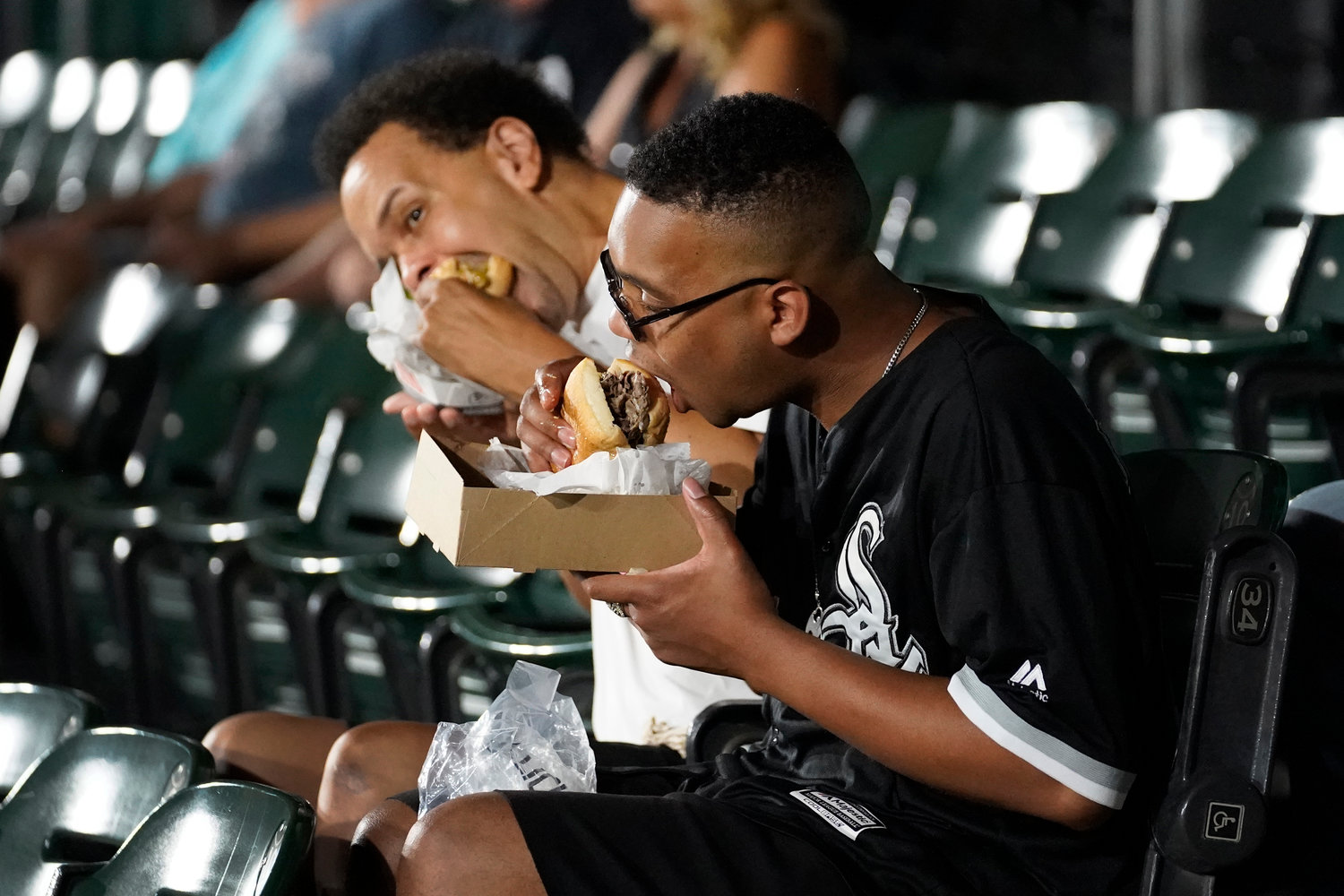 Aaron Armstead, left, and his son Alec, from Chicago, take bites out of their sandwiches before a September baseball game between the Cleveland Guardians and Chicago White Sox in Chicago. Persistently high inflation and gas prices are looming over sports and the monetary pipeline that resumed when fans returned to games amid the pandemic.