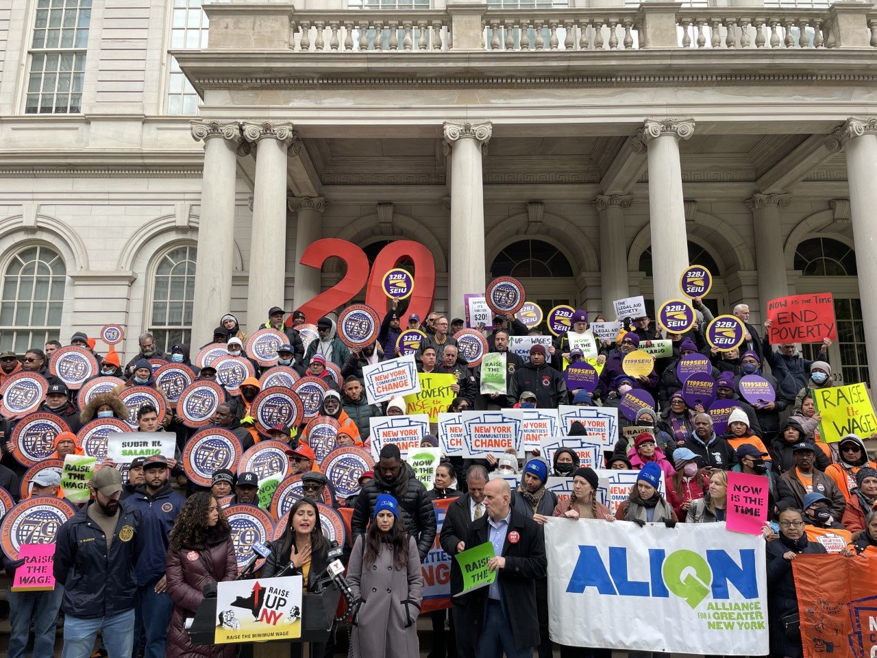 State Senator Jessica Ramos, at the microphone, joined by union leaders, workers and advocates on the City Hall steps Tuesday, announced that she would be introducing legislation to raise the state's and the city's minimum wage.