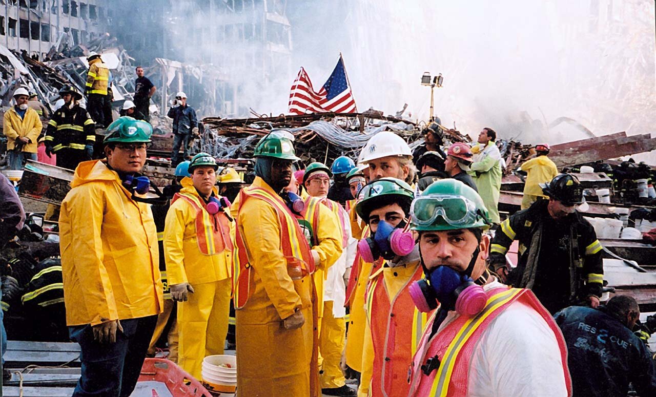 NYC Transit Authority workers at ground zero. Alongside first responders and others, they labored to find the remains of the dead out of a sense of duty, one of them, Philip Ronnie Shpiller, pictured at right rear behind the U.S. flag, said recently. He and 38 of his colleagues have been shut out of three-quarter disability payments granted thousands of others who also worked on the pile.