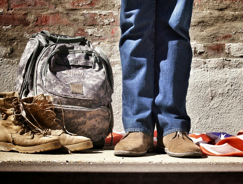 Stock photo of military gear with someone standing off to the right and an American flag sprawled out behind the person's legs.