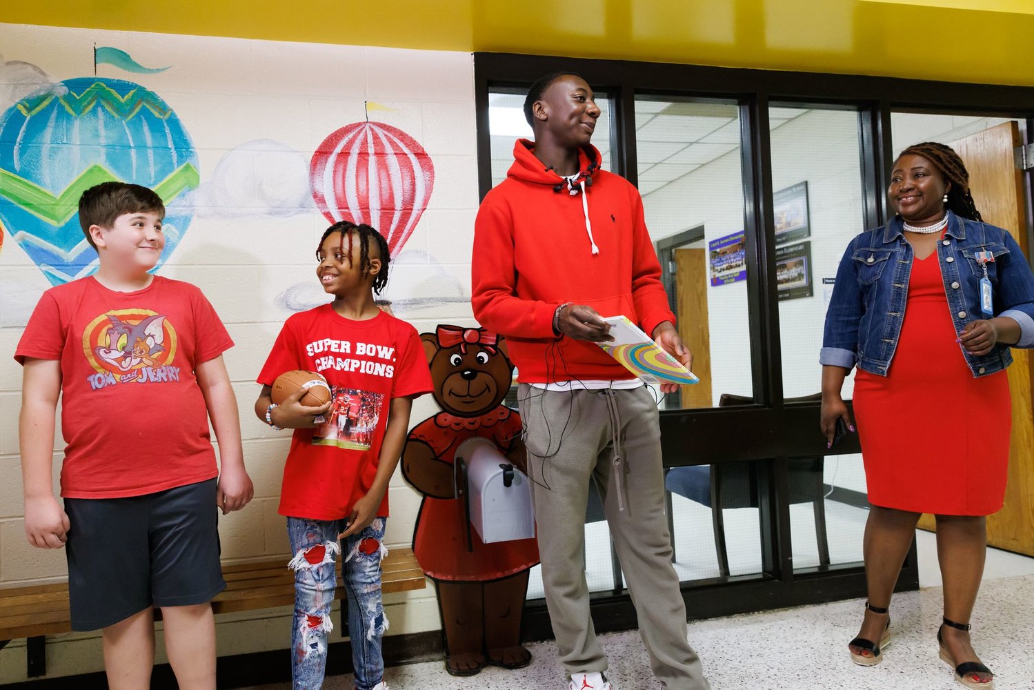 Super fans David Mikkels, left, and Justin Malloy stand with Kansas City Chiefs star Joshua Williams as Principal Tara Bratcher looks on at Loyd Austin Elementary School on Thursday.