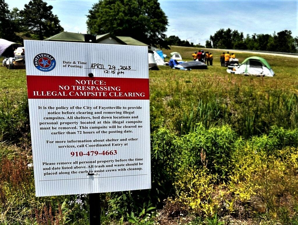 A sign posted at a homeless camp on state-owned property at Gillespie Street and the Martin Luther King Jr. Freeway includes a telephone number that the homeless can call for temporary help.