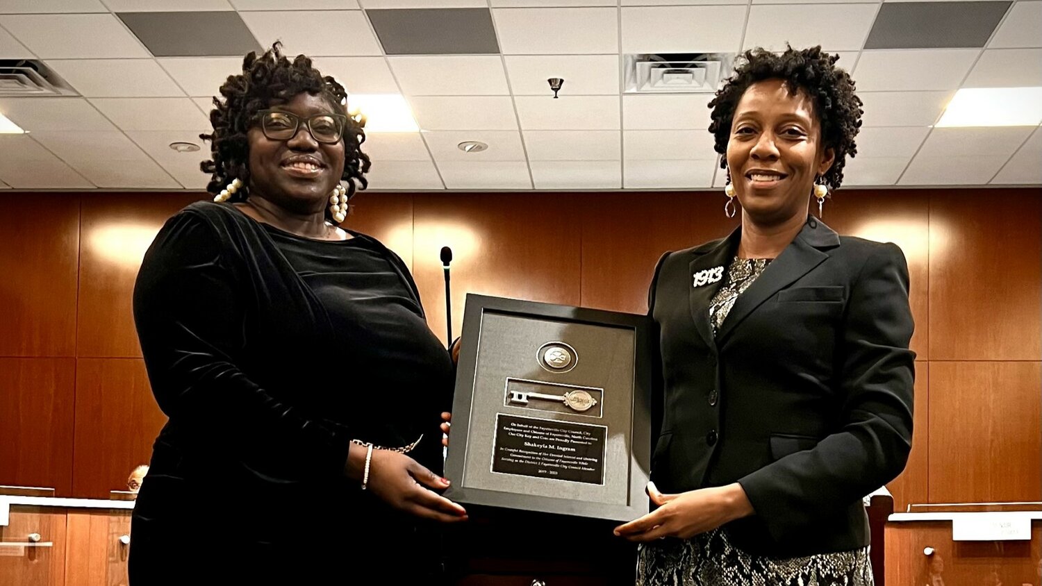 Councilmember Shakeyla Ingram accepts a symbolic "key to the city" from Councilmember Courtney Banks-McLaughlin, who gave a farewell speech recognizing Ingram's work on the council.