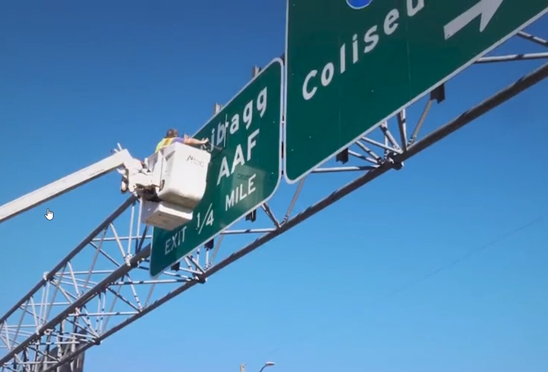 A screen capture from a video of a worker installing a “Fort Liberty” panel on a road sign that previously said “Fort Bragg” on Skibo Road near the All-American Freeway in November 2023.