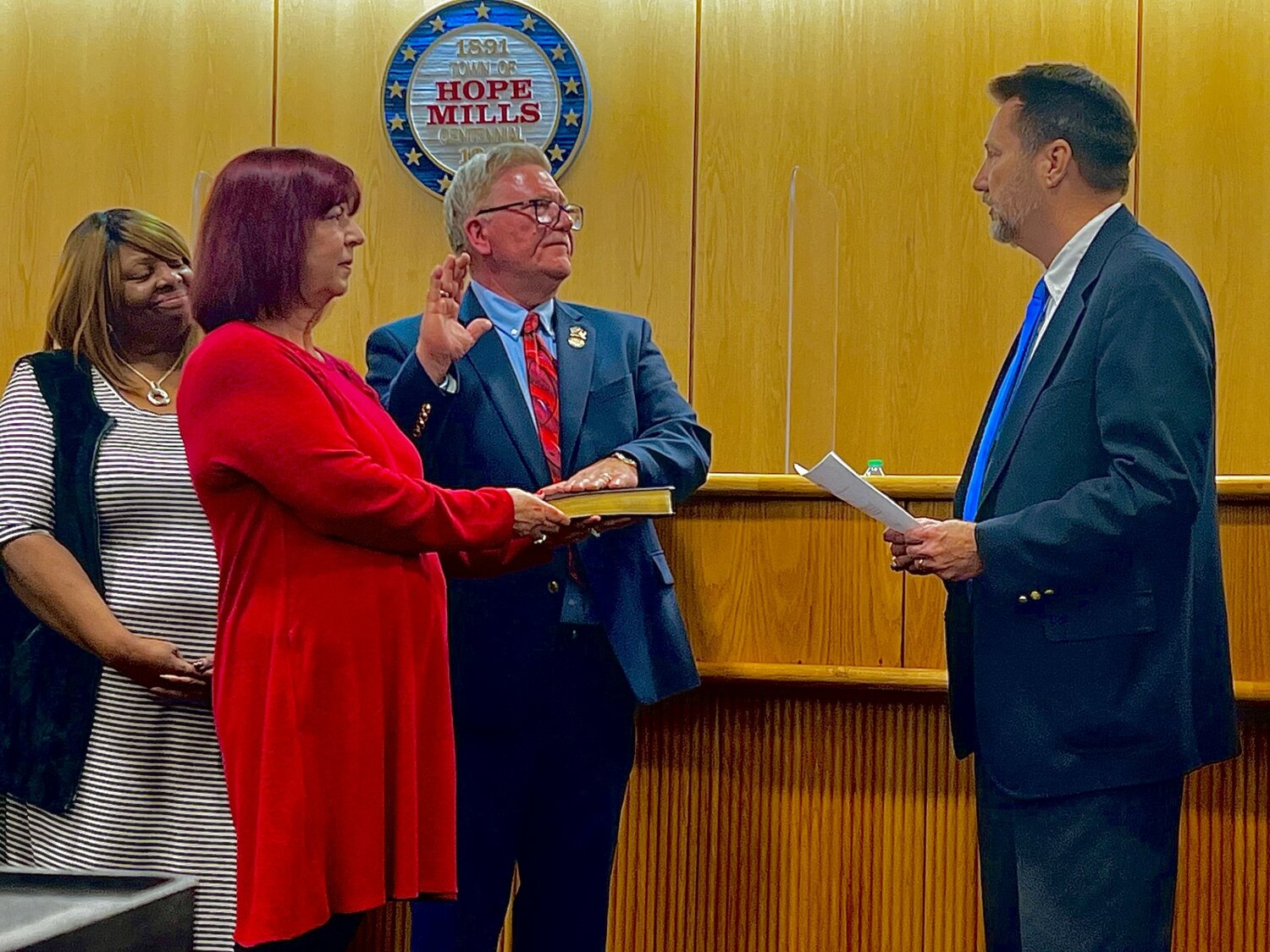 Bambi Bellflowers (red dress) holds a Bible while Jessie Bellflowers is sworn in as the new mayor of Hope Mills by Senior Resident Superior Court Judge James Floyd Ammons Jr. (right) at Monday night's Hope Mills Board of Commissioners meeting.