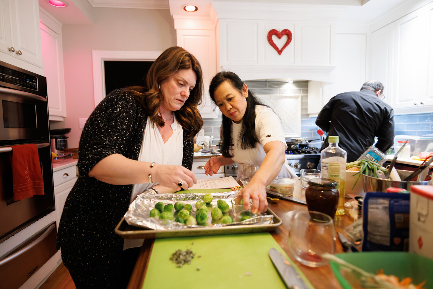 Barbara Wise (left) learns Chef Mai's smashing technique for her Crispy Smashed Brussels sprouts while her husband Brian begins sauteing squash for the Winter Squash Risotto with Sage and Pine Nuts.
