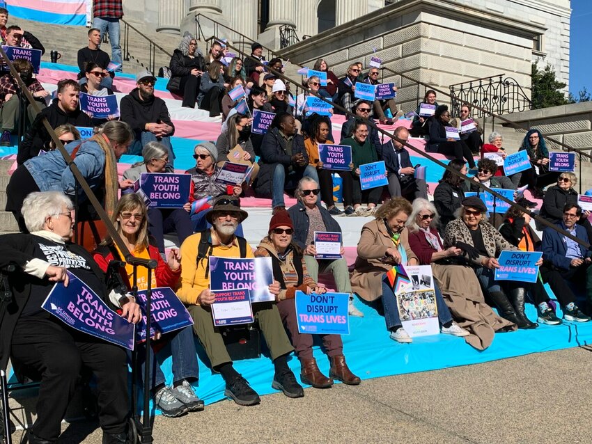 Activists gather on the Statehouse steps with signs and transgender flags Wednesday, Jan. 10, 2024. A Senate committee advanced a bill that would ban gender transition surgery, hormone therapy and puberty-blocking drugs for minors Thursday. (Skylar Laird/SC Daily Gazette)