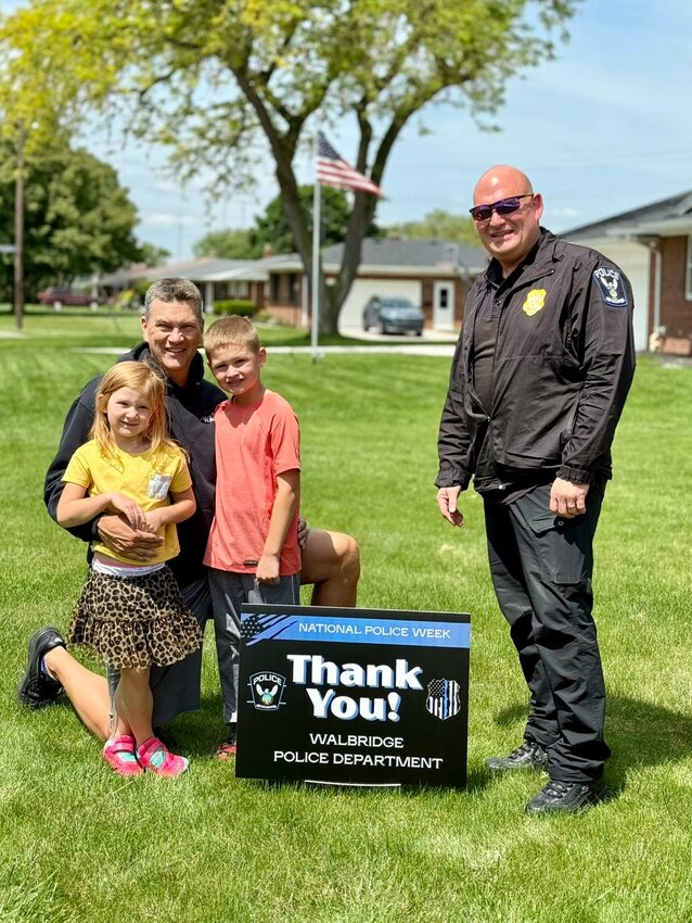 Walbridge police chief Ken Campbell (right) and Walbridge mayor Ed Kolanko (left) are pictured with Kolanko's children behind one of the signs the village is giving away to interested residents.