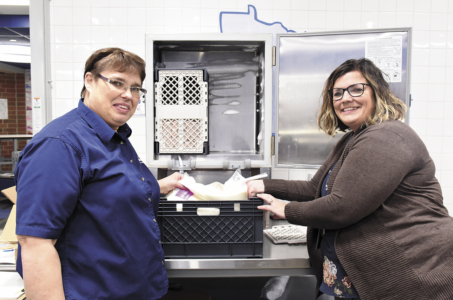 Director of food service Patty Viaene (left) and principal Laura Spanier prepare to add a 50-pound bag of milk to one of the milk dispenser machines Nov. 9 at Belgrade-Brooten-Elrosa High School in Belgrade, Minnesota. During the school’s adjustment from milk cartons to dispensers, various staff, including Spanier, have stepped in to help change bags during lunchtime.