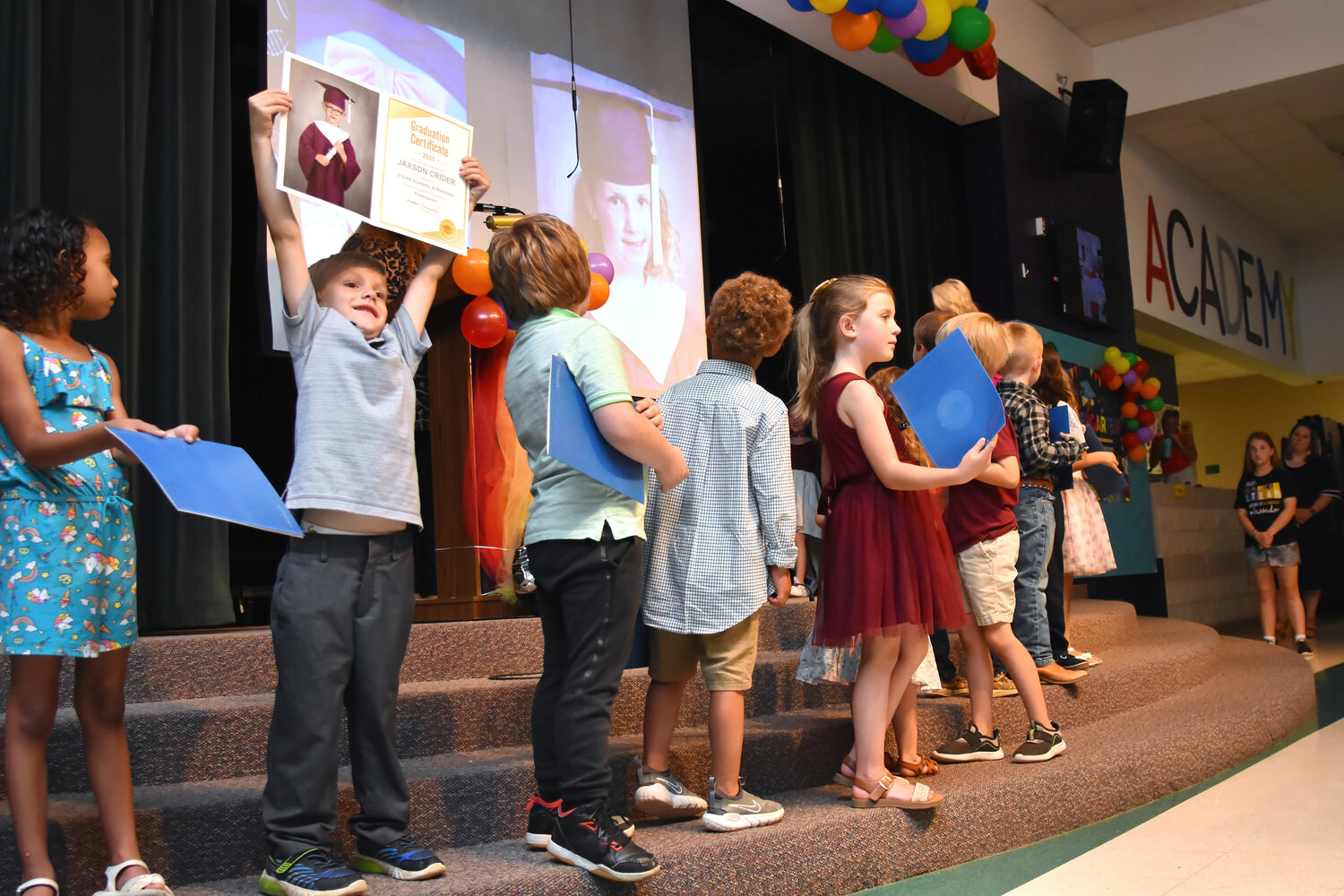 Kindergarten graduate Jaxson Crider, second from left, proudly shows off his graduation certificate to mom and dad during the STEAM Academy at Mambrino ceremony on May 22. 