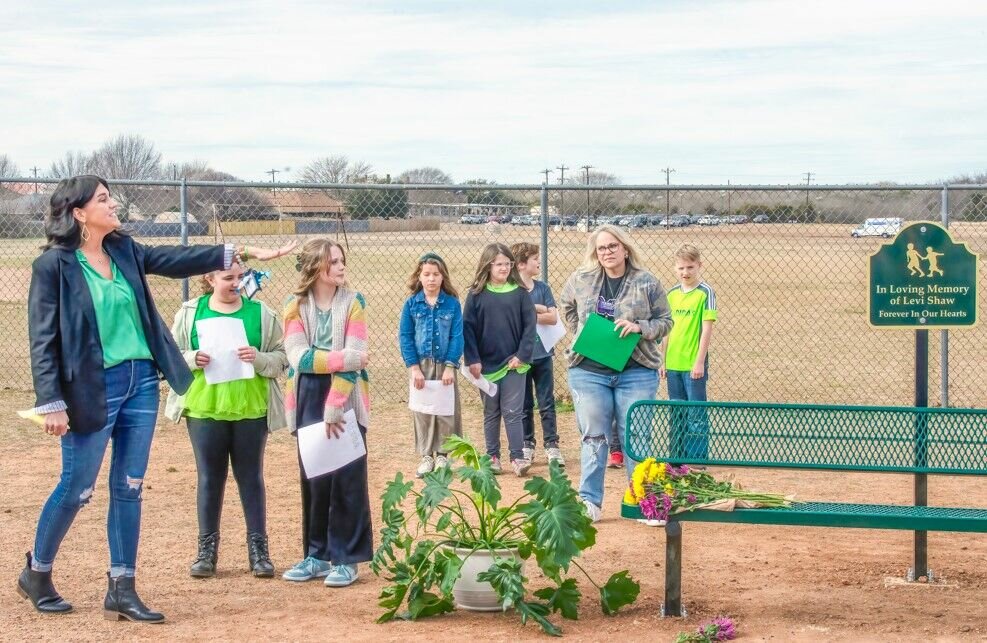 A memorial was held at Brawner Elementary School last Friday for 9-year-old Levi Shaw, who passed away last August. In honor of his memory, a “Buddy Bench” was installed at the Brawner playground. During the memorial, Sandy Ruiz, far left, assistant principal at Brawner Elementary School, talks about the "Buddy Bench,” while Levi’s closest friends prepare to deliver speeches about their beloved classmate.
