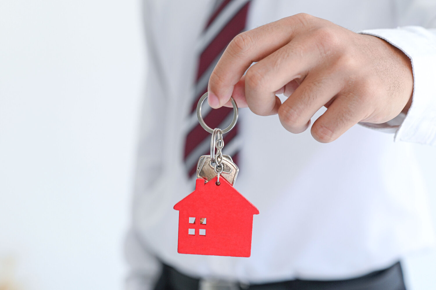 Male hand holding a keychain with model house, real estate trading concept, real estate insurance, close-up photo.