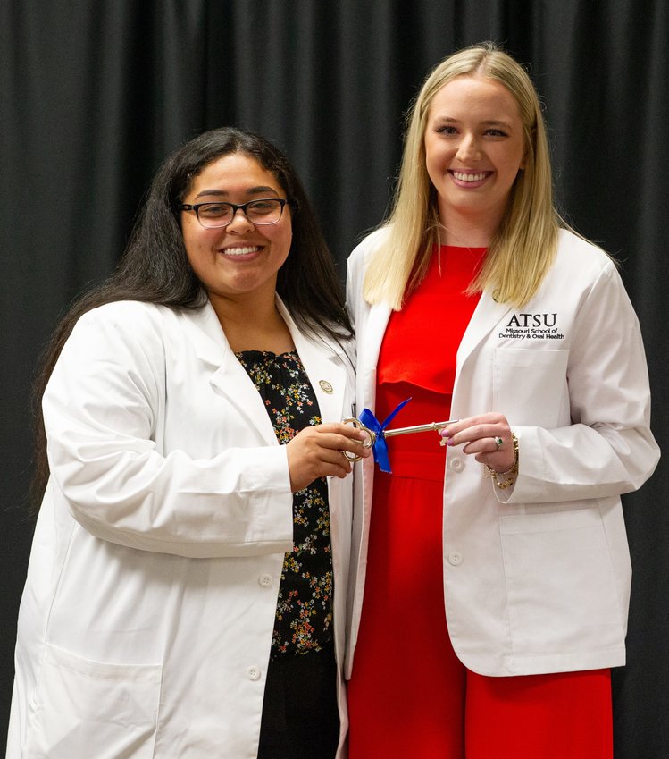 Second-year A.T. Still University-Missouri School of Dentistry &amp;amp; Oral Health student Destiny Mills, left, presents a symbolic key to first-year ATSU-MOSDOH student Ashley Ingram during the White Coat Ceremony. The annual transfer represents the key to A.T. Still's log cabin and symbolizes the obligation first-year students have in preserving ATSU's heritage.