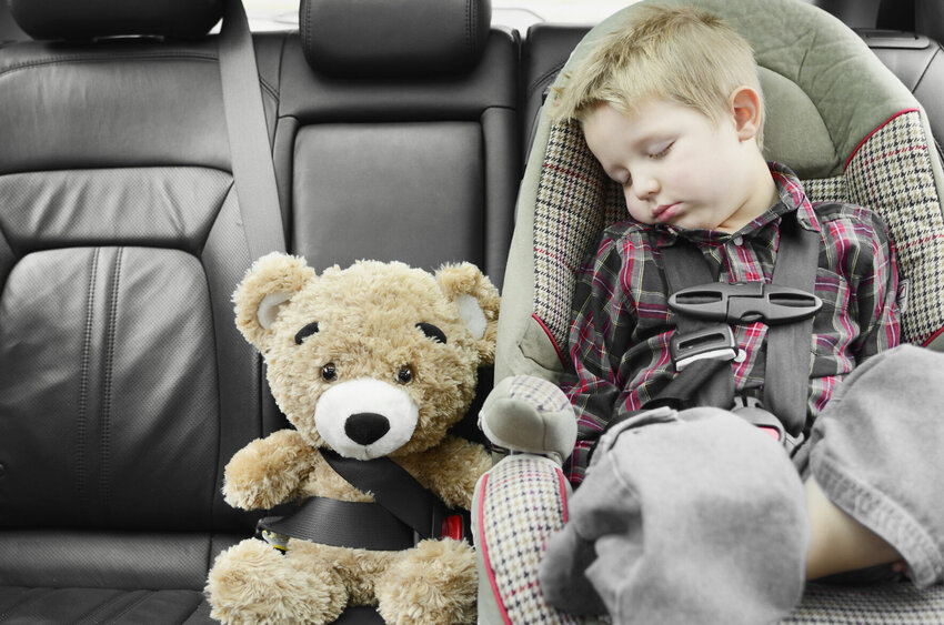 Child sound a sleep seating in the car seat next to buckled up teddy bear, safety first. Shallow DOF, natural light.