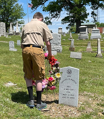 A boy scout lays a wreath next to the new gravestone.