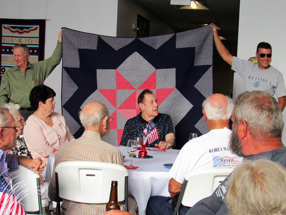 A quilt is presented to Charles Bud Elam, seated in front of his quilt.