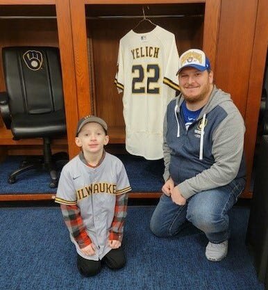 Owen Strege of Algoma kneels in front of Christian Yelich's locker in the Milwaukee Brewers locker room with his uncle, Jeremy Kruse of Green Bay, during a ceremony Feb. 18 at American Family Field where he and two other youths with pediatric health issues learned they and their families would travel to the Brewers spring training camp in Phoenix and throw out the first pitch for the team's Feb. 25 game against the Los Angeles Dodgers.