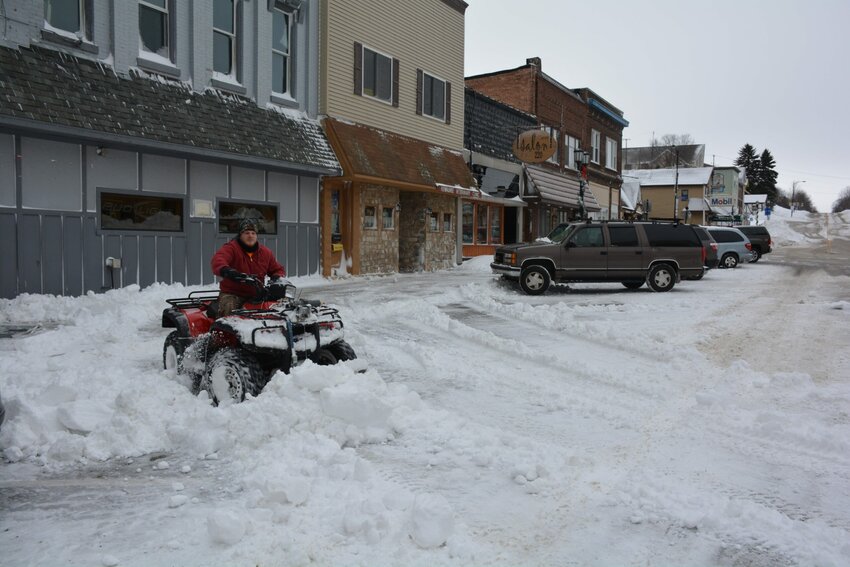 Tyler Slack, owner of Kewaunee Bowl, uses his ATV to clear parking spaces in front of his downtown Kewaunee building.