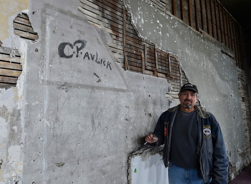 Tom Skubal stands next to the "C. Pavlick'' signature he discovered under the wall layers in the Selner Plumbing & Heating building. The autograph was likely made in the 1930s.