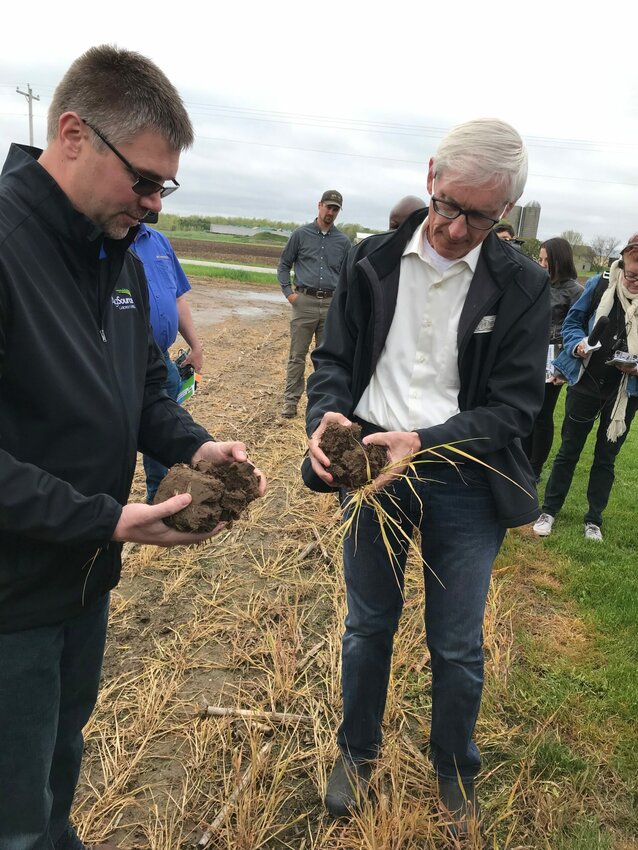 Nick Guilette of AgSource Laboratories, left, shows Gov. Tony Evers chunks of soil that were planted with a cover crop of rye to help prevent water runoff and erosion at Deer Run Dairy in Kewaunee.