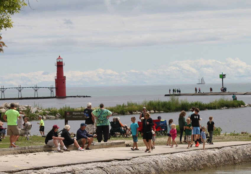 A tall ship on the horizon sails past Algoma Pierhead Lighthouse as people gather on Crescent Beach.