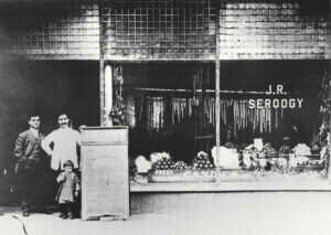 Rookoos and Anastasia Seroogy's sons, Jim and Joe, stand in front of a Seroogy's storefront. The young girl pictured with them is Helen Seroogy Shalhoub, Joe's daughter and mother of actor Tony Shalhoub. Seroogy's photo