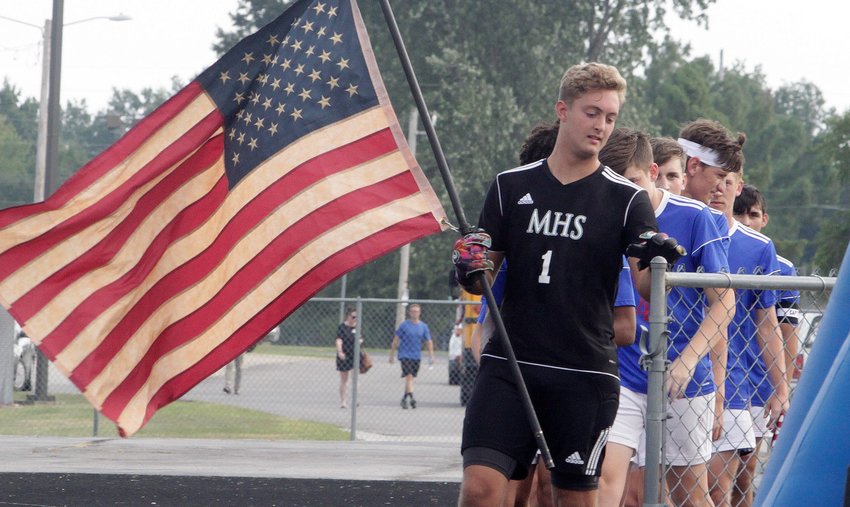 Moberly senior Noah Lucas carries an American Flag as he leads the varsity soccer team into the home grandstands Tuesday evening at Dr. Larry K. Noel Spartan Stadium prior to the playing of the national anthem. The honorable gesture was part of a memorial tribute for the 13 U.S. Soldiers that were killed Aug. 26 as they helped scores of people to safety when two terrorist suicide bombers and gunmen attacked the gathering of people at the Kabul, Afghanistan airport.