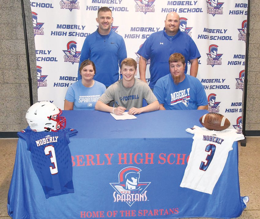 Moberly football player Dakotah Courtney (center) smiles while his parents, Ashley and Jonathan Long, Spartan head football coach Cody McDowell and athletic director Curtis Walk surround him. Courtney has signed to play football at the University of Dubuque in Iowa.