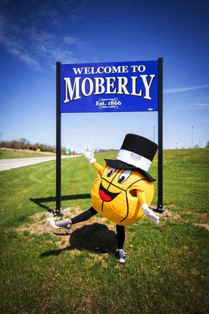 The Gus Macker basketball mascot stands in front of a Welcome to Moberly road sign announcing his Sept. 25-26 arrival to Moberly to become part of a busy weekend of events having a 3-on-3 tournament played here.