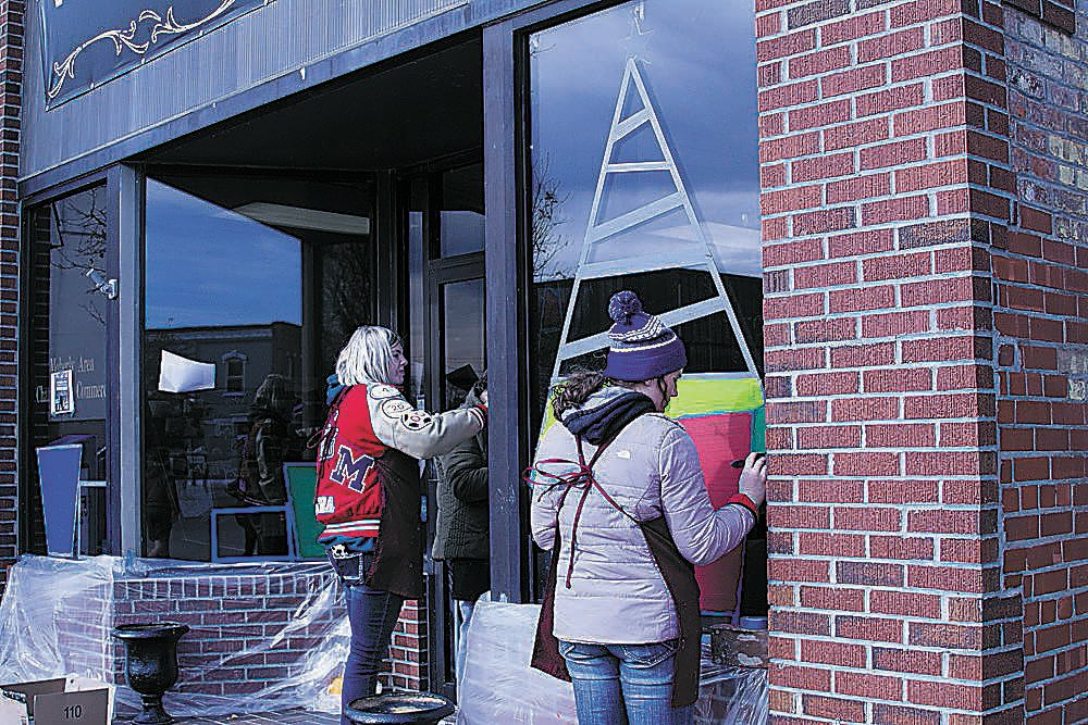 Students paint a festive Christmas scene of the windows of the chamber of commerce office.