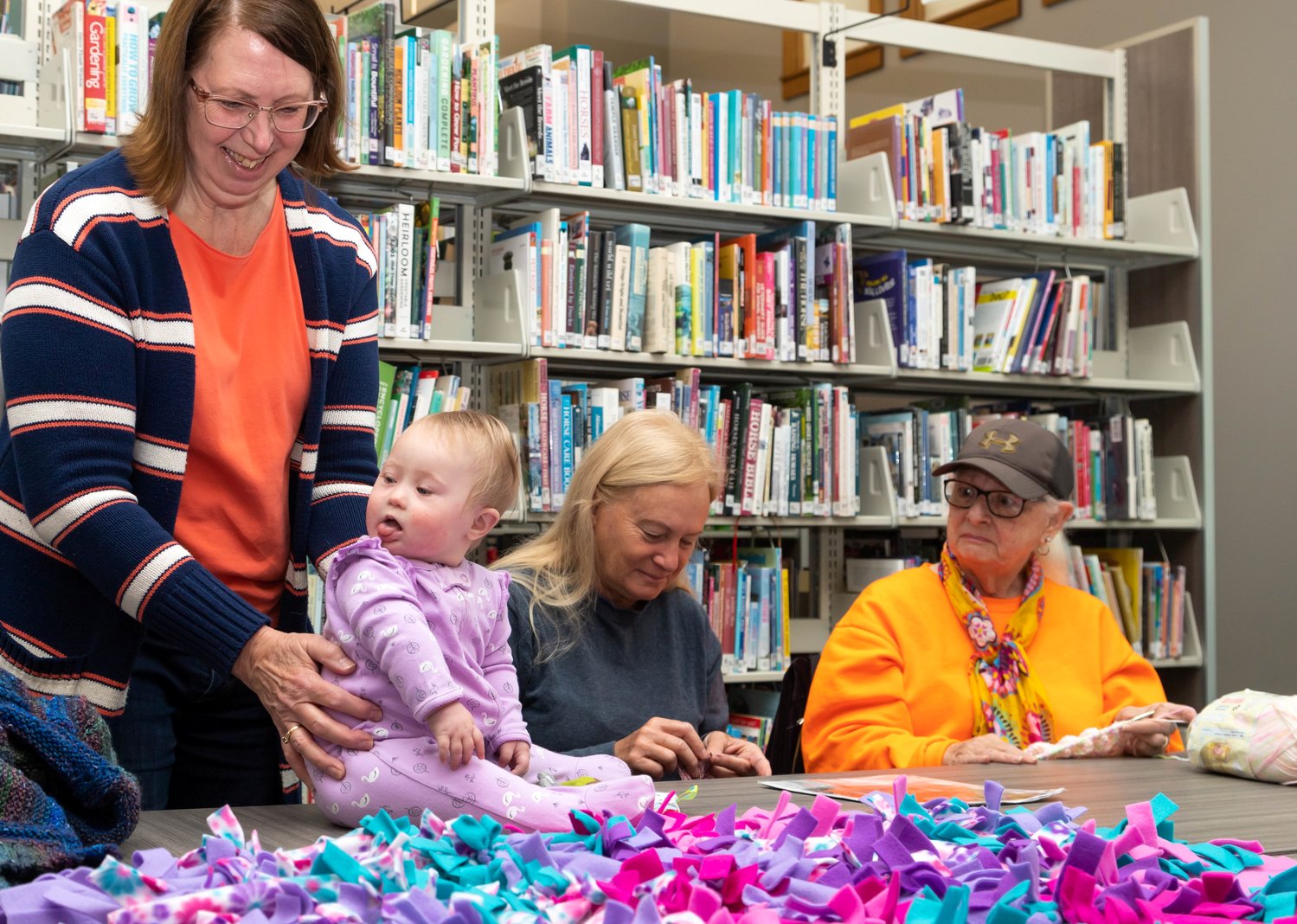 Baby Brielle Stoldt sits on a table surrounded by knitters and crocheters. From left are Diane Benner, Brielle, Annie Kershaw and Linda Wheeler.