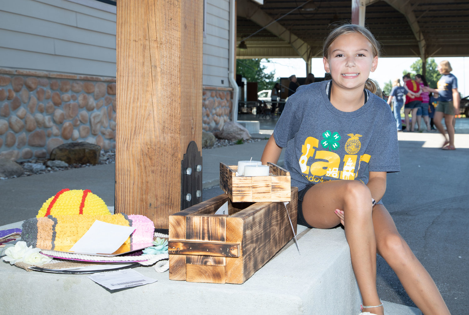 Kensley Goble, of Huntsville, sits among the projects she submitted for judging Monday at the Randolph County Fair in Moberly’s Rothwell Park. Goble decorated two foam cakes and created a wood planter and a decorative candle holder.