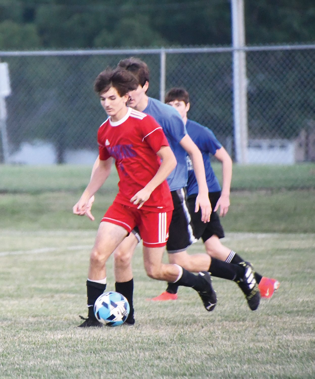 Spartan soccer player Jordan Rasico (red jersey) dribbles with the ball while a pair of Boonville players trail him during a showcase scrimmage on Wednesday, July 27, at Moberly High School.