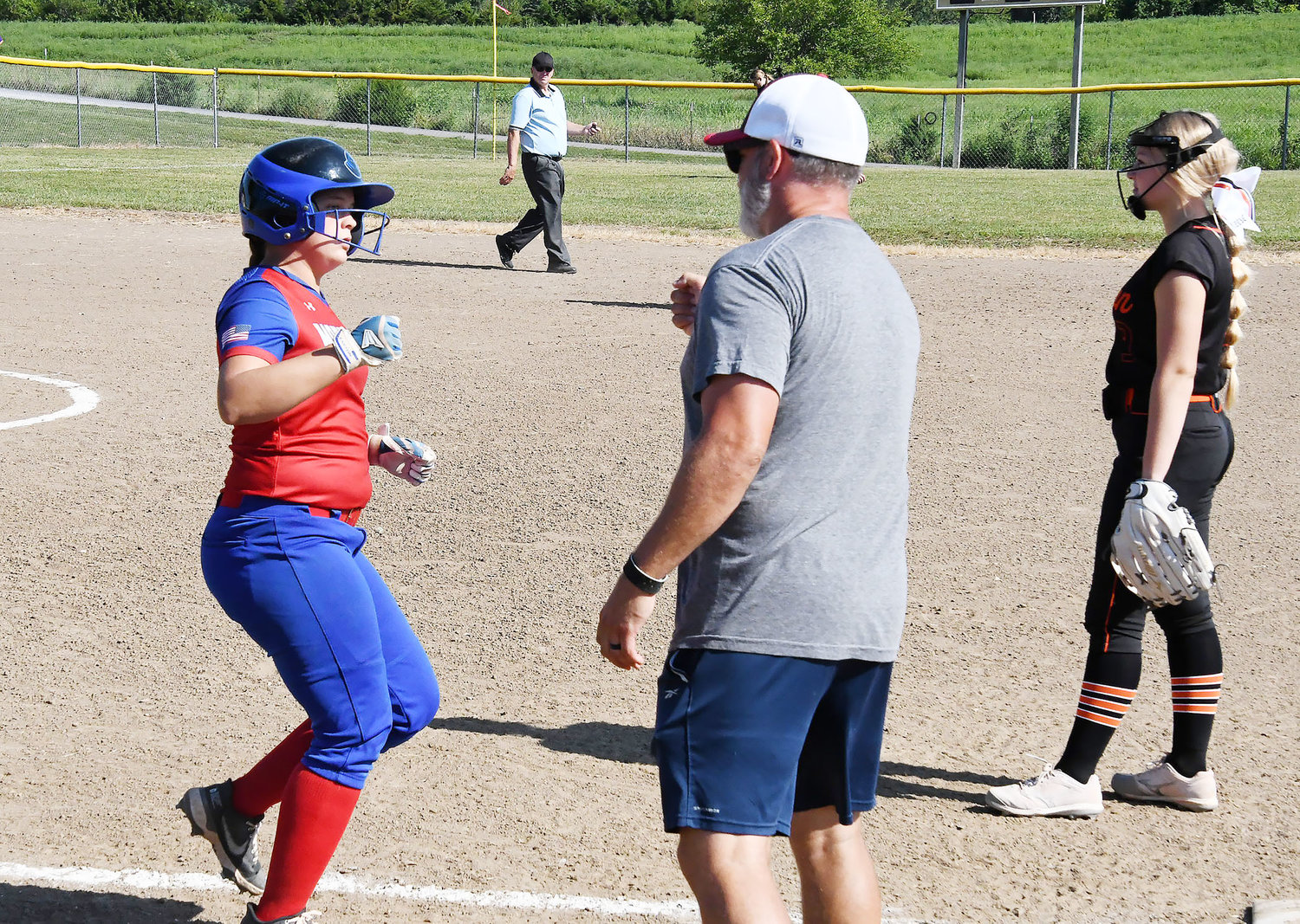 Moberly's Jordan Pasbrig is congratulated by Spartan assistant coach Dale Heimann at first base. Macon's Reece Adair and umpire Bob Roberts also are photographed.
