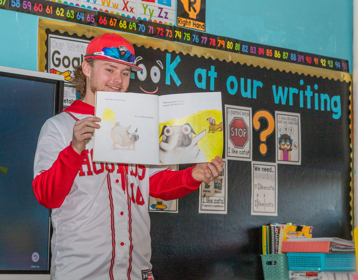Greyhound pitcher Clayton Ello shows a St. Pius kindergarten class photos from the book “Pig the Pug/Fibber” during Catholic School Week. Baseball players read to students as part of Favorite Sports Team day.