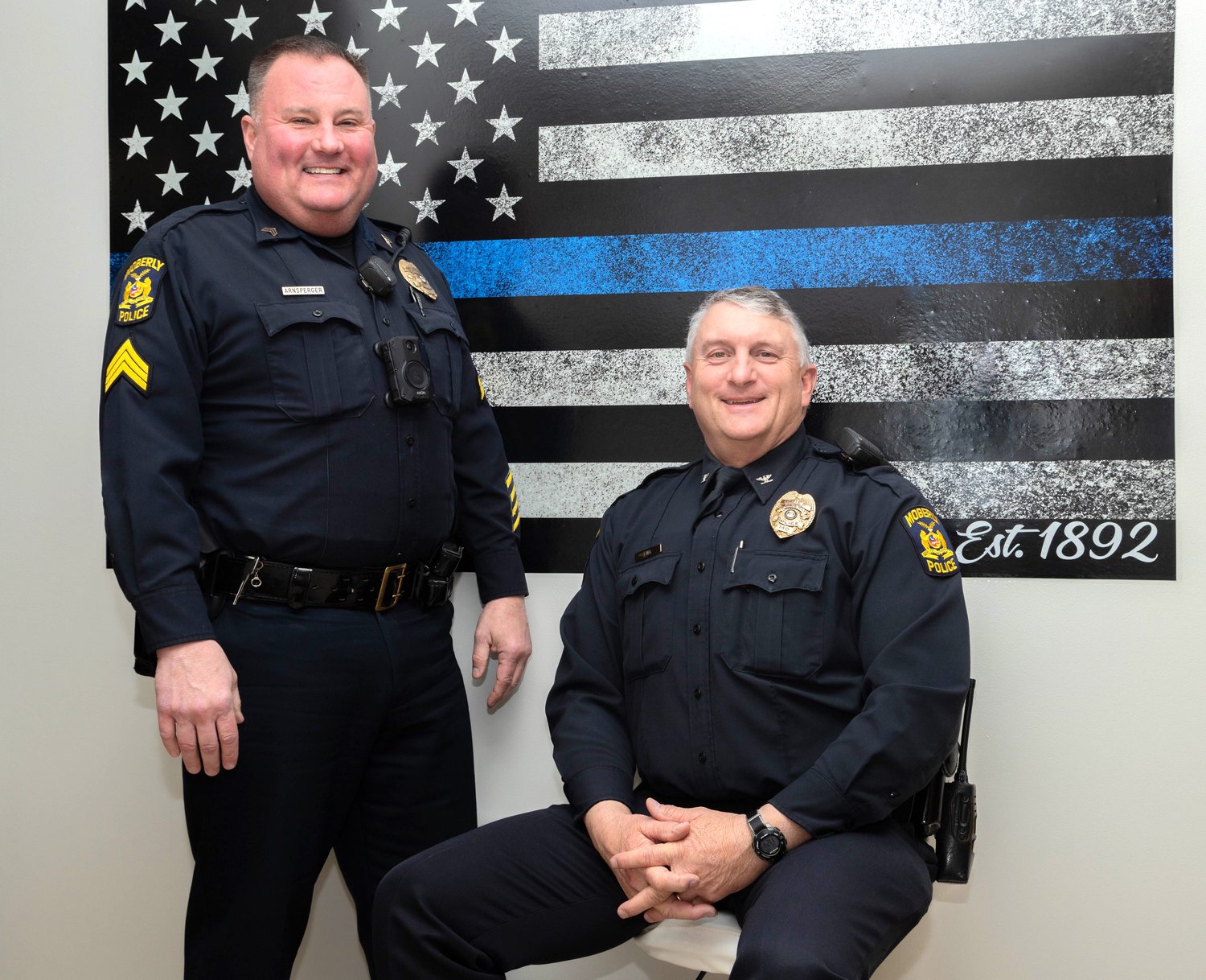 Sgt. Mark Arnsperger and Moberly Police Chief Troy Link pose in front of a Back the Blue flag at Moberly Police Department. The two began their careers with Moberly PD more than 30 years ago.