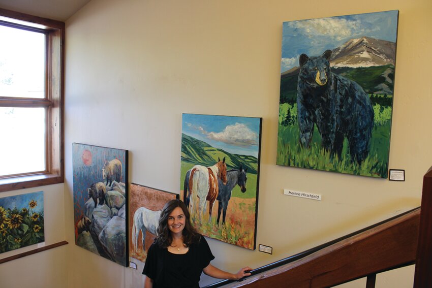 Studio Tour Allenspark — The Old Gallery: 
Artist Malena Hirschfeld poses next to a handful of her paintings near the second floor inside The Old Gallery.