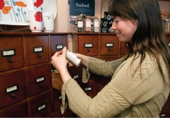 Ambrosia owner Claudia Butler examines one of the many types of salt the shop offers, and stores in cabinets resembling a library’s card catalog.