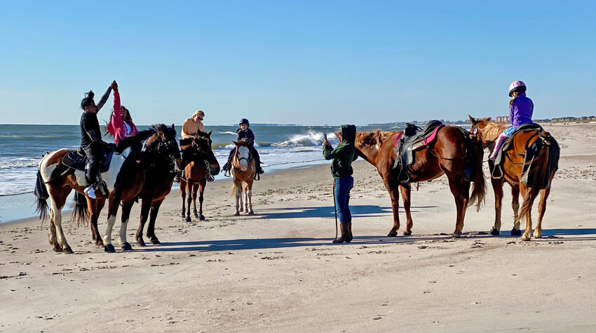 A group of horse riders pose for photos on the beach.