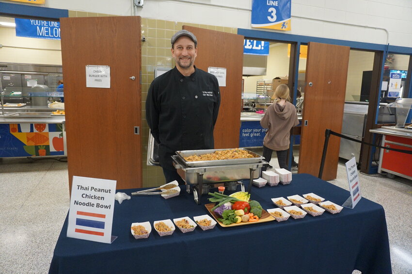 Chef Mike Damos stands with his table before the middle school lunchroom serving Thai peanut chicken noodle bowls.
