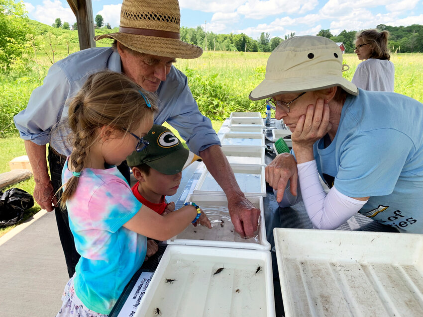 Dr. Dean Hanson (retired from the University of Minnesota) and Heidi Sundet, Ellsworth Public Library Clerk, assist Jack and Isla Thayer at the Ellsworth Public Library&rsquo;s Trimbelle Nature Day, held last year at the Trimbelle Rec Area off County Road O.