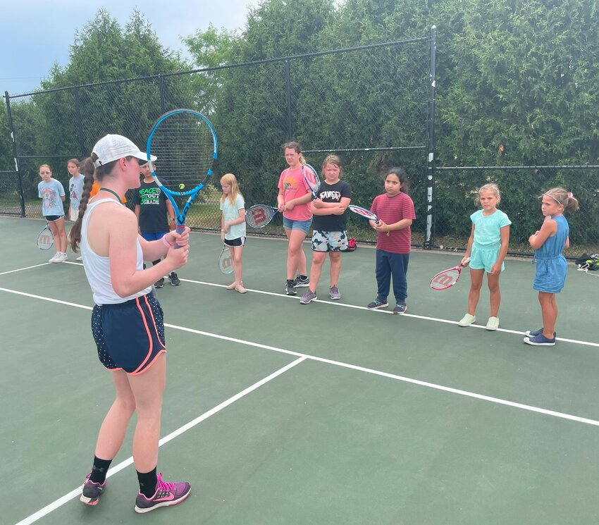 An instructor teaches the basics of tennis to kids at youth tennis camp.