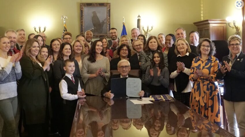 Surrounded by advocates including students, teachers and legislators, Gov. Tony Evers displays the signed law that requires Wisconsin high school students study financial literacy.