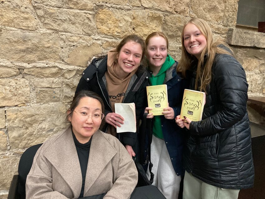 College Lit seniors Sienna McCoy, Lauren Meyer, and Delania Kurtz pose with Kao Kalia Yang alongside her book The Song Poet.